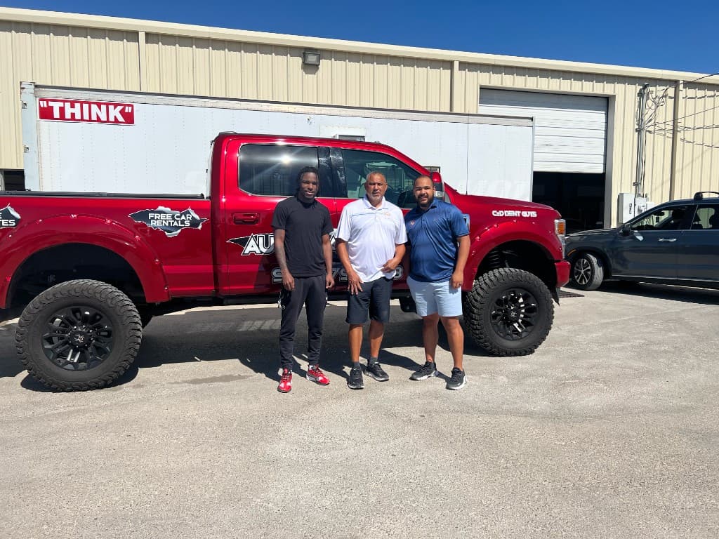 Carlos and the C & D Dent Guys team standing in front of the branded red truck